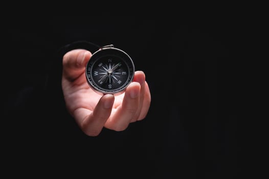 A woman's hand holds a compass showing south on a black background. A hand from the darkness holds out a compass, the concept of being lost and finding a solution or ideas with meanings