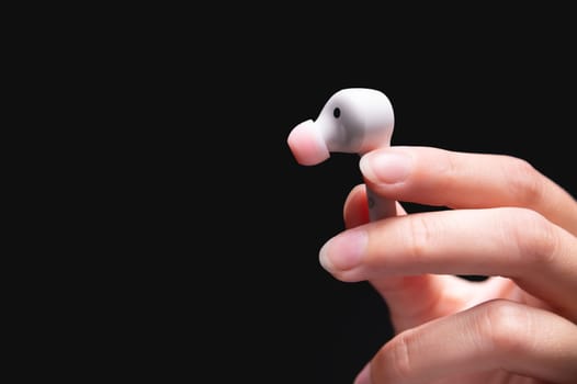 White wireless earphone in a woman's hand. Close up of vacuum earphone held in hand on dark background.