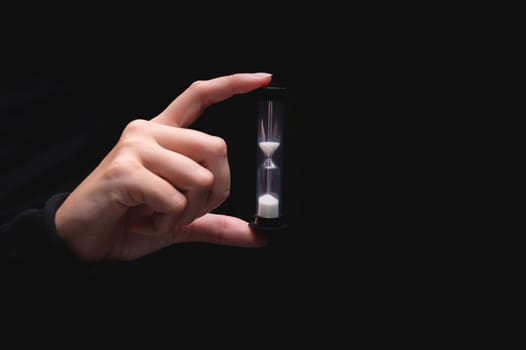 Close-up of a woman holding an hourglass. Time goes by and time runs out. Countdown timer.