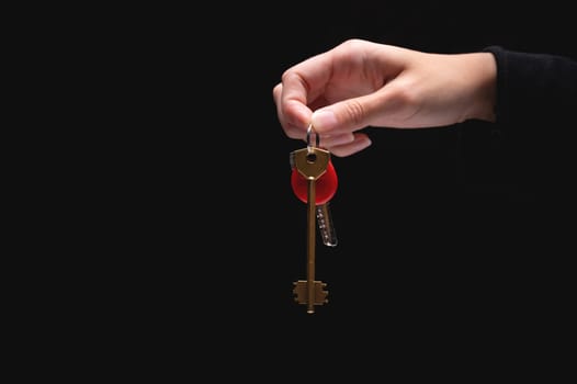 A hand holds the keys to the apartment on a black background. Young adult woman holding metal door keys in her hand, close-up. Blank space for text.