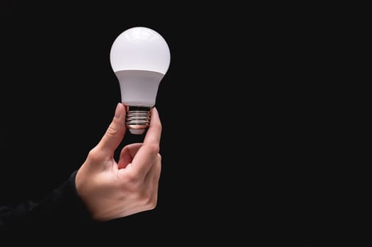 light bulb in hand on a black background. Close-up of a woman's hand holding a light bulb. Studio shot.