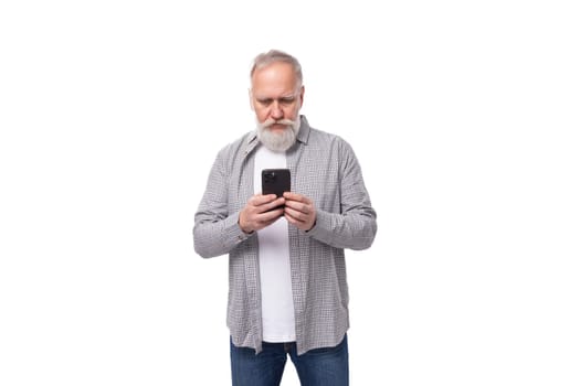 a handsome pensioner man with a beard and a big mustache is dressed in a shirt and jeans chatting on the phone.