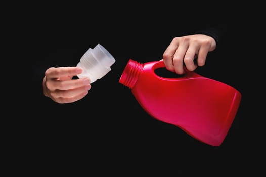 A woman's hand pours cleaning product or bleach on a black background. Woman opened detergent, close-up, label mockup
