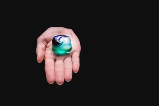 Washing capsules in hands. Washing powders for washing clothes in a washing machine, on a black background. Purity concept.