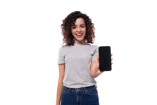 well-groomed caucasian young brunette woman with curly hair shows smartphone screen on white background with copy space.