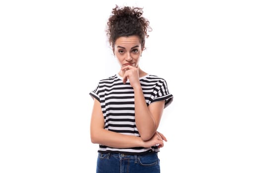 young smart caucasian woman with curly black hair dressed in a striped black and white t-shirt looks puzzled and thoughtful.