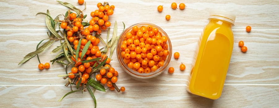 Sea buckthorn healthy drink in bottle, ripe berries in glass jar and branches with leaves top view on white wooden rustic background, great for skin, heart, vessels and immune system..