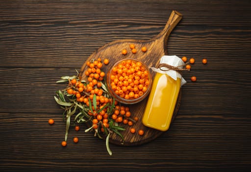 Sea buckthorn healthy drink in bottle, ripe berries in glass jar and branches with leaves top view on dark wooden rustic background, great for skin, heart, vessels and immune system..