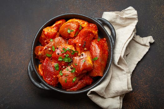 Raw uncooked chopped pieces of meat marinated with seasonings and parsley in black casserole dish top view on dark rustic background. Cooking ragout stew with marinated meat fillet pieces.