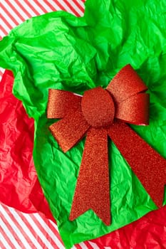 This is a photo of a red glitter bow on a green crumpled tissue paper with a red and white striped background
