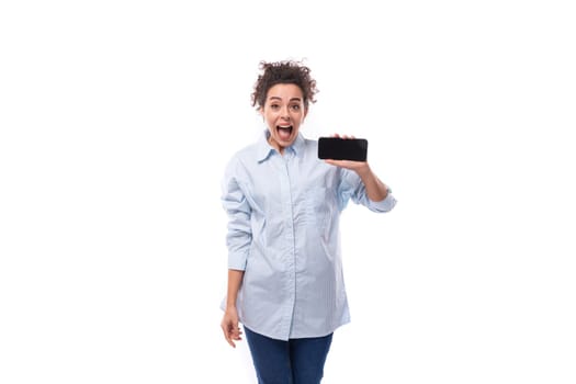 young pretty curly brunette secretary woman oeta in a light blue shirt holds a smartphone screen forward.