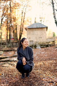 Young smiling woman squatting in autumn park and looking away. High quality photo