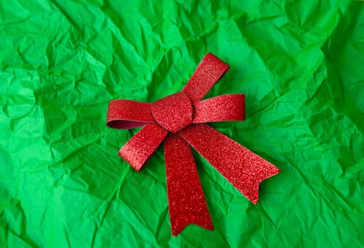 A photo of a red glittery bow on a green crumpled paper background. The bow is in the center of the image and the background fills the frame
