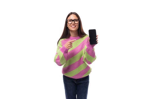 young beautiful caucasian woman with straight black hair with glasses is dressed in a stylish autumn striped pullover shows a smartphone screen mockup.