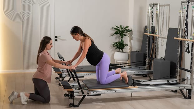 A pregnant woman works out on a reformer exercise machine with a personal trainer