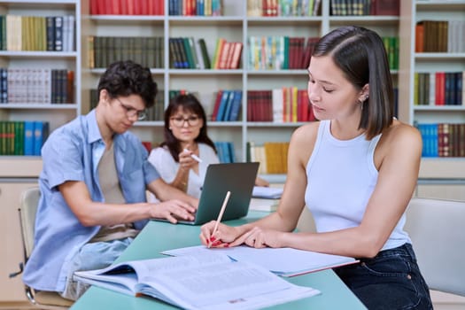 Portrait of student girl at desk inside college library, male student together with teacher preparing for exam. Knowledge, education, youth, college university concept