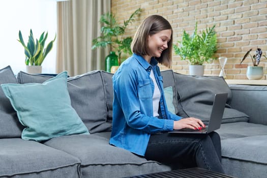 Young woman sitting on sofa typing on laptop. Internet technologies for study leisure, female freelancer working remotely, university student watching online course, e-learning, rest communication