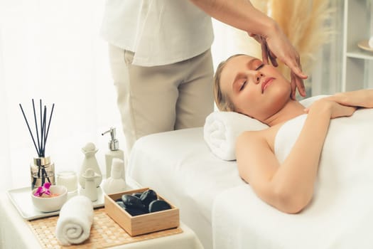 Caucasian woman enjoying relaxing anti-stress head massage and pampering facial beauty skin recreation leisure in dayspa modern light ambient at luxury resort or hotel spa salon. Quiescent