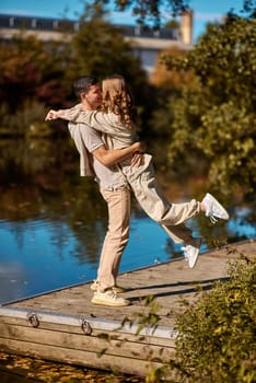 A happy couple in love in casual clothes travel together, hike and have fun in the fall forest on a weekend in nature in autumn outdoors, selective focus. Handsome man embracing with passion his girlfriend outdoor under the leaves of trees on the embankment. Love history. Happy people concept