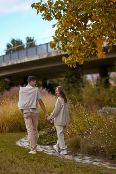 Young couple in love walking in the autumn park holding hands looking in the sunset. Closeup of loving couple holding hands while walking at sunset. The hands of the male and female lovers who hold hands walk forward high with blurred background