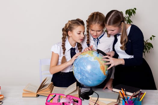 three schoolgirl girls with books and a globe in geography class at the desk