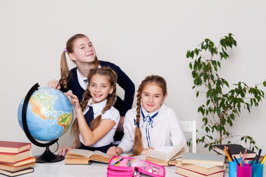 three schoolgirl girls with books and a globe in geography class at the desk