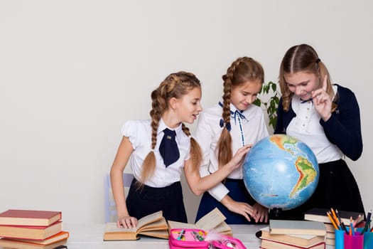 three schoolgirl girls with books and a globe in geography class at the desk