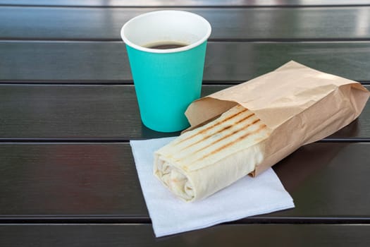 a glass of coffee and shawarma in lavash on the table. photo