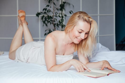 blonde woman reads a book in the bedroom on the bed