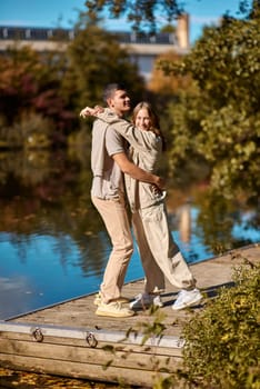A happy couple in love in casual clothes travel together, hike and have fun in the fall forest on a weekend in nature in autumn outdoors, selective focus. Handsome man embracing with passion his girlfriend outdoor under the leaves of trees on the embankment. Love history. Happy people concept