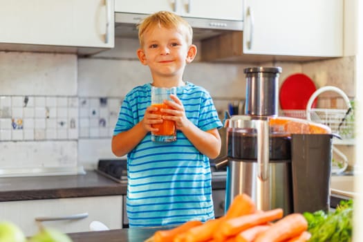 Little boy drinking freshly squeezed carrot juice from a glass in the kitchen. Concept of healthy and delicious food