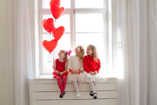 Three beautiful little girls with balloons in red and white dresses at the party