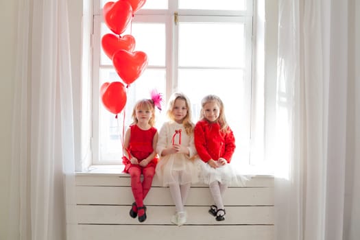 Three beautiful little girls with balloons in red and white dresses at the party