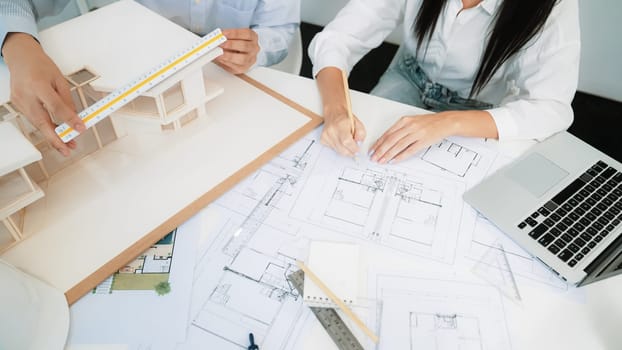 Professional engineer measures house model while skilled designer writes down in blueprint. Work together, collaboration, cooperate. Creative design and team working concept. Closeup. Immaculate