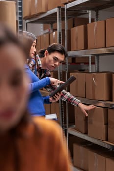 Warehouse employees inspecting parcels on rack and doing inventory management. Storehouse asian package handler and supervisor checking goods maintenance on shelf in storage room