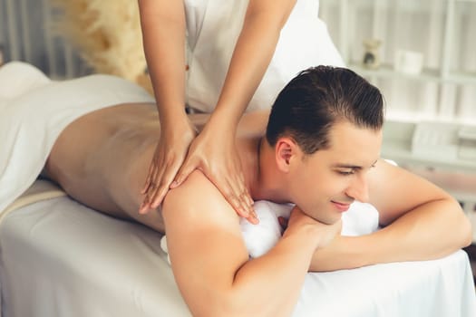 Caucasian man customer enjoying relaxing anti-stress spa massage and pampering with beauty skin recreation leisure in day light ambient salon spa at luxury resort or hotel. Quiescent