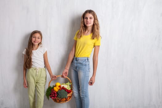 Two girls holding a basket of ripe vegetables