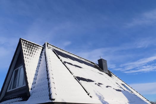 Snow covered solar panels producing clean energy on a roof of a house