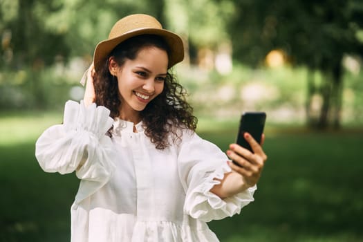 Young beautiful girl in a hat makes a selfie on her phone in the park. High quality photo