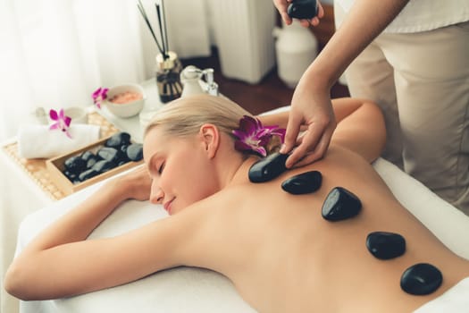 Hot stone massage at spa salon in luxury resort with day light serenity ambient, blissful woman customer enjoying spa basalt stone massage glide over body with soothing warmth. Quiescent