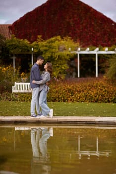A couple in love hugs on the shore of a city pond in the European town. love story against the backdrop of autumn nature. romantic ambiance, couple goals, outdoor romance, seasonal charm, love in the city, autumnal vibes, European town, city pond, affectionate bonding, love story