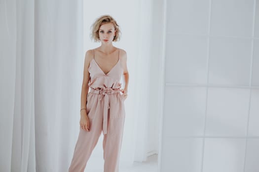 Portrait of a beautiful fashionable blonde woman in a pink jumpsuit in a white room