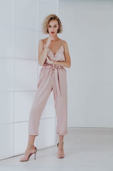 Portrait of a beautiful fashionable blonde woman in a pink jumpsuit in a white room