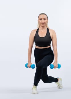 Full body length shot active and sporty senior woman lifting dumbbell during weight training workout on isolated background. Healthy active physique and body care lifestyle for pensioner. Clout