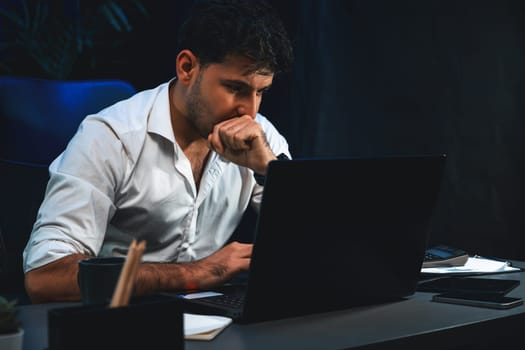 Stressful businessman using laptop to analyze database information of marketing planer, sending email to coworker or customer at workplace. Concept of remote working online at night time. Sellable.