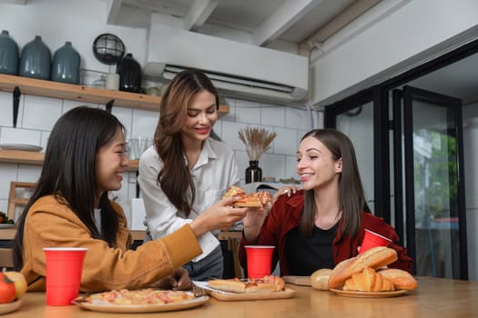 A group of young female friends have a party with pizza on the table and red drink glasses. Talk and live together happy, having fun at home..