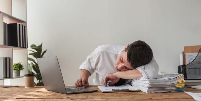 Unhappy young office worker feeling bored at work looking at laptop with a hopeless expression while sitting in the office. Male office worker feeling tired from monotonous work..