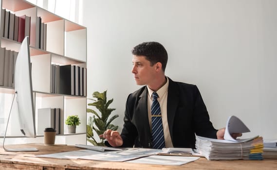 Unhappy young businessman feeling bored and stressed at work looking at laptop with hopeless expression while sitting in office.