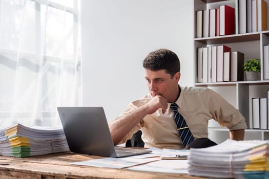 Unhappy young businessman feeling bored and stressed at work looking at laptop with hopeless expression while sitting in office.