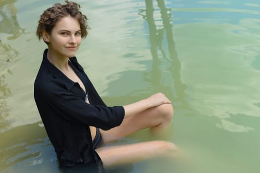 Young woman in a dark dress sits in the water.